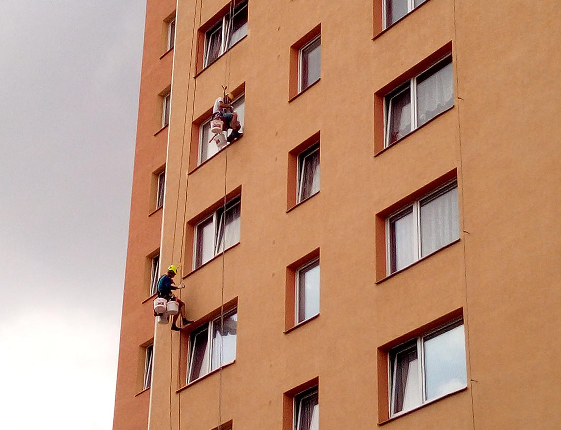 Fotografie dvou výškových pracovníků na fasádě panelového domu